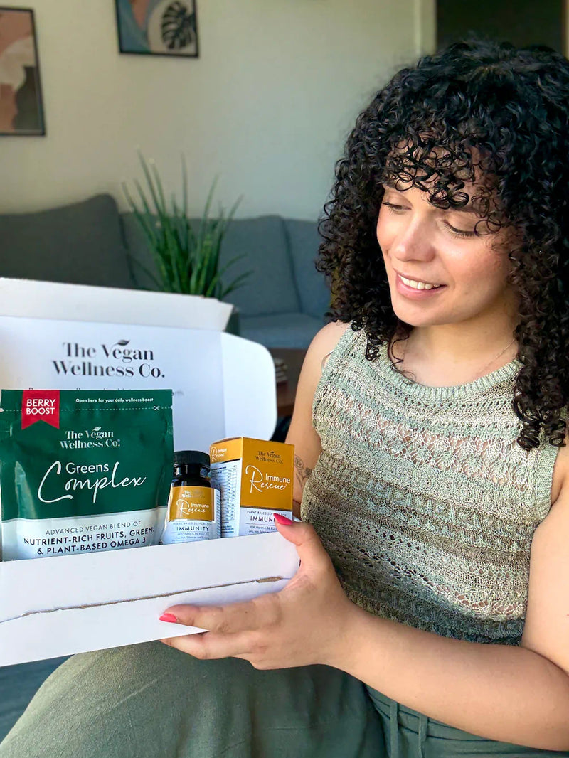 Woman holding a box from The Vegan Wellness Co. with health products inside.