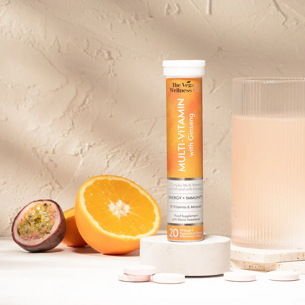 Multivitamin supplement tube with an orange, passion fruit, and glass of water on a neutral background