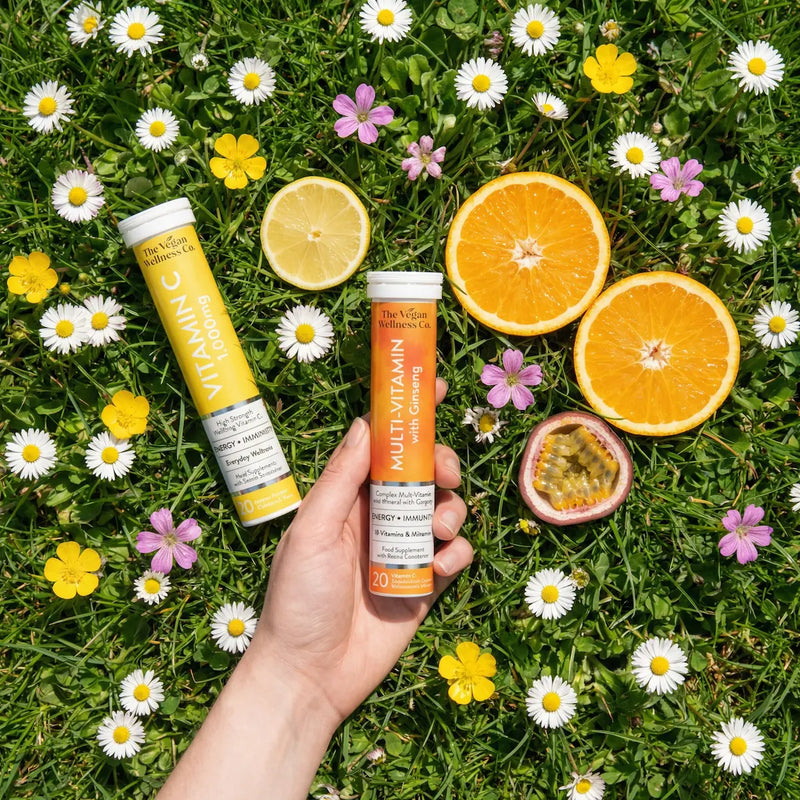 Hand holding a multivitamin supplement tube with fruits and flowers on grass