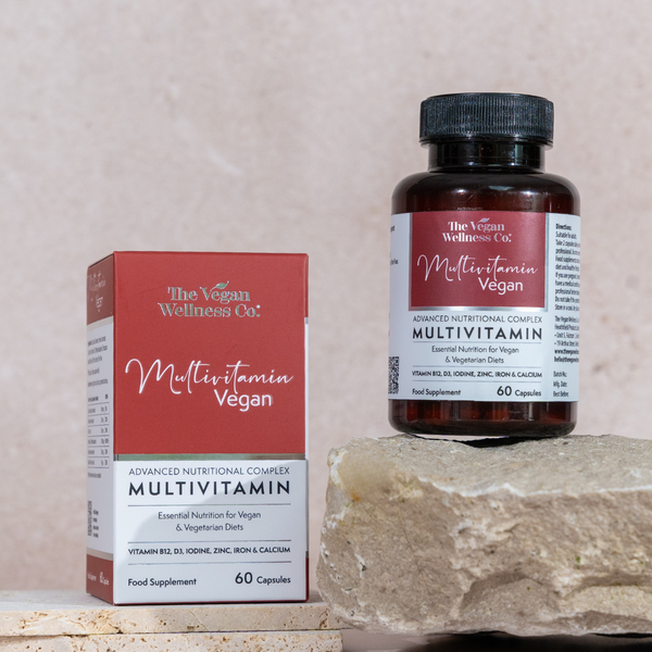Multivitamin bottle and packaging from The Vegan Wellness Co. on a stone surface with a neutral background